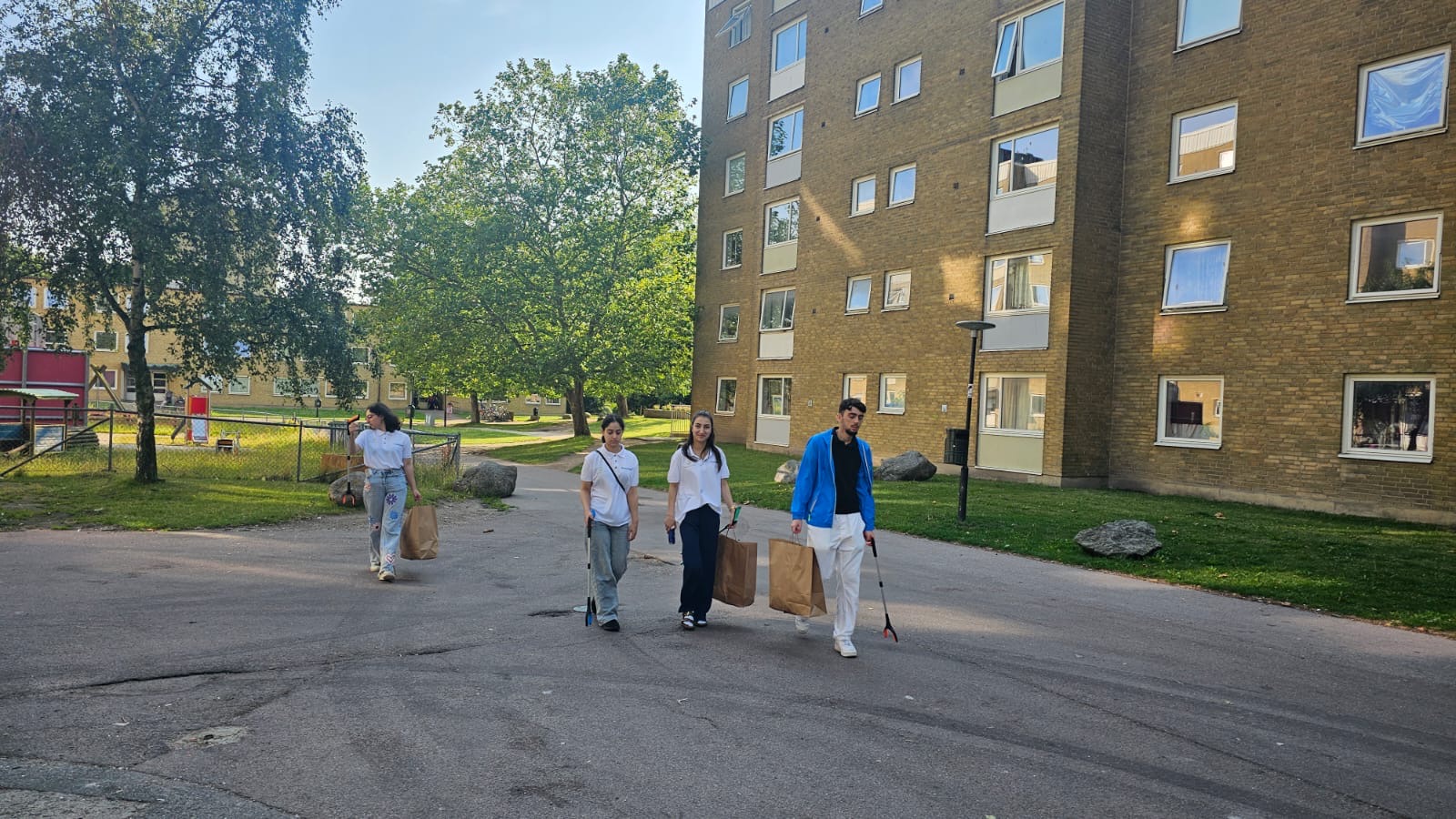 Medlemmar i Miljöambassadörer går tillsammans genom ett bostadsområde med skräpplockare och papperspåsar efter en städaktivitet.